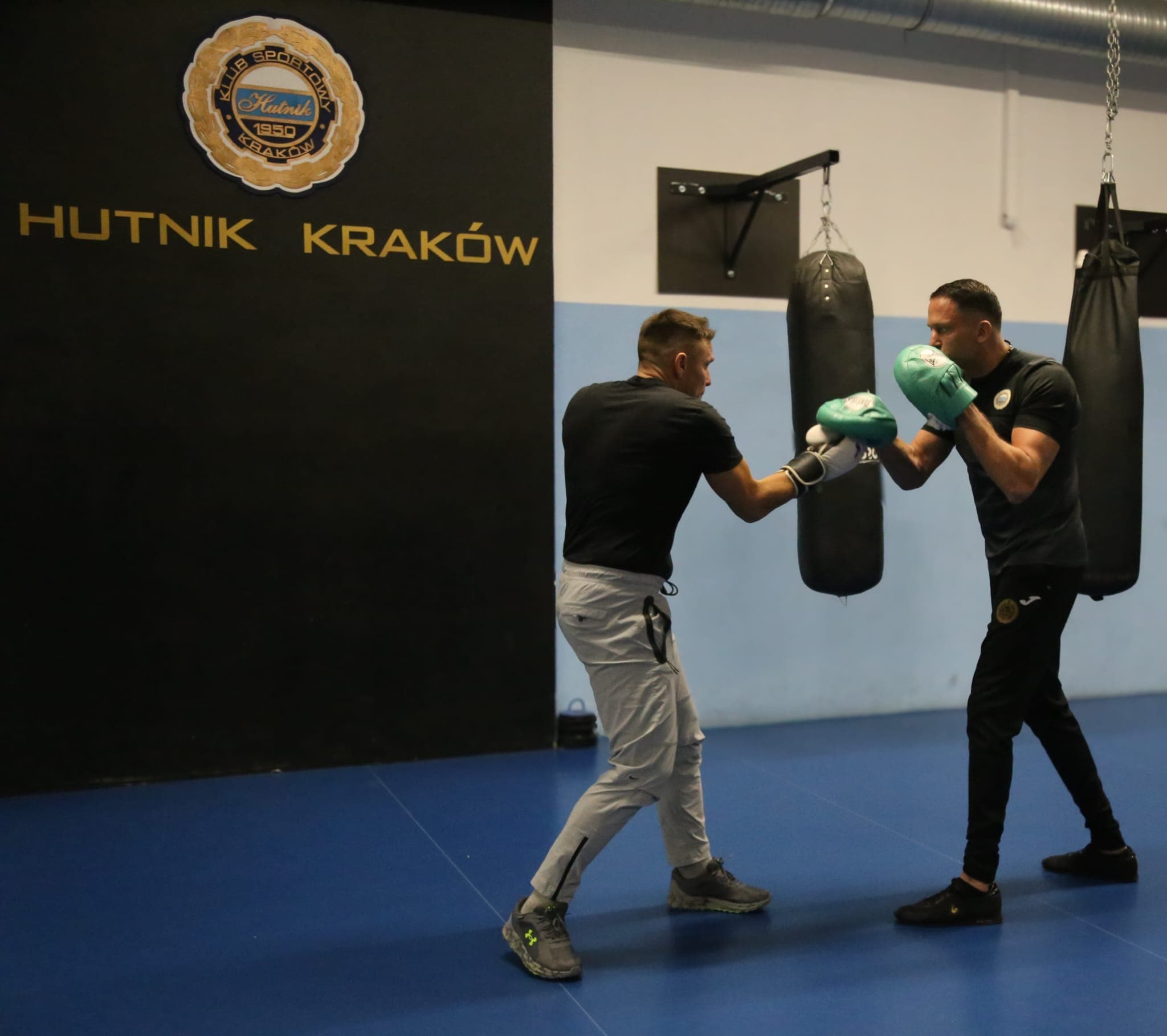 Trening bokserski na łapach w sali Hutnika Kraków z logo klubu na ścianie
